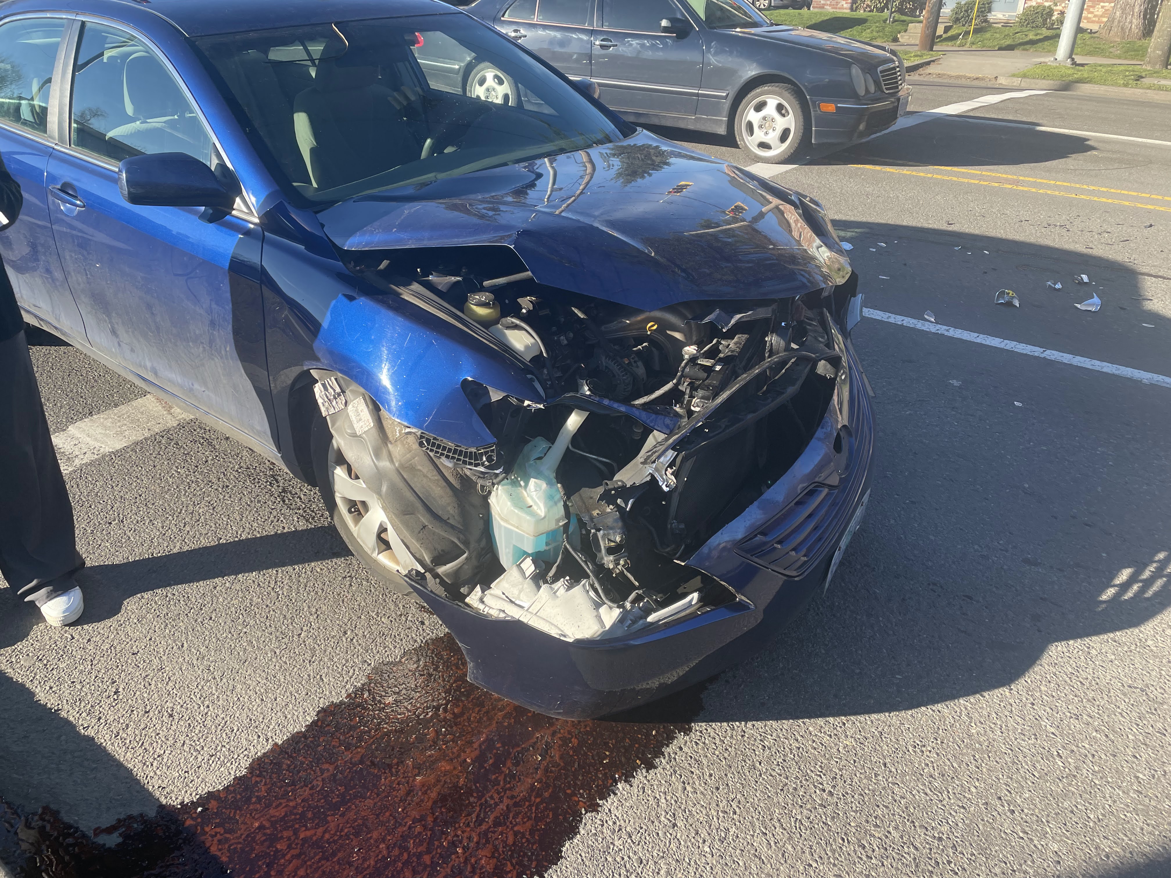 Photo of my car that I took at the scene, the front bumper is mostly off and liquids are draining into the road.