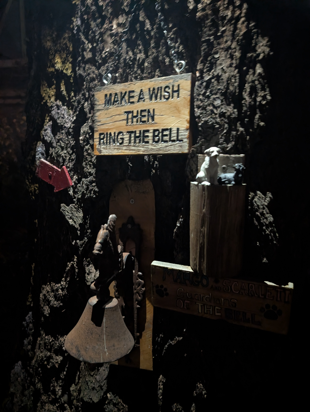 A sign on a tree above an old bell, which reads, "Make a wish then ring the bell."